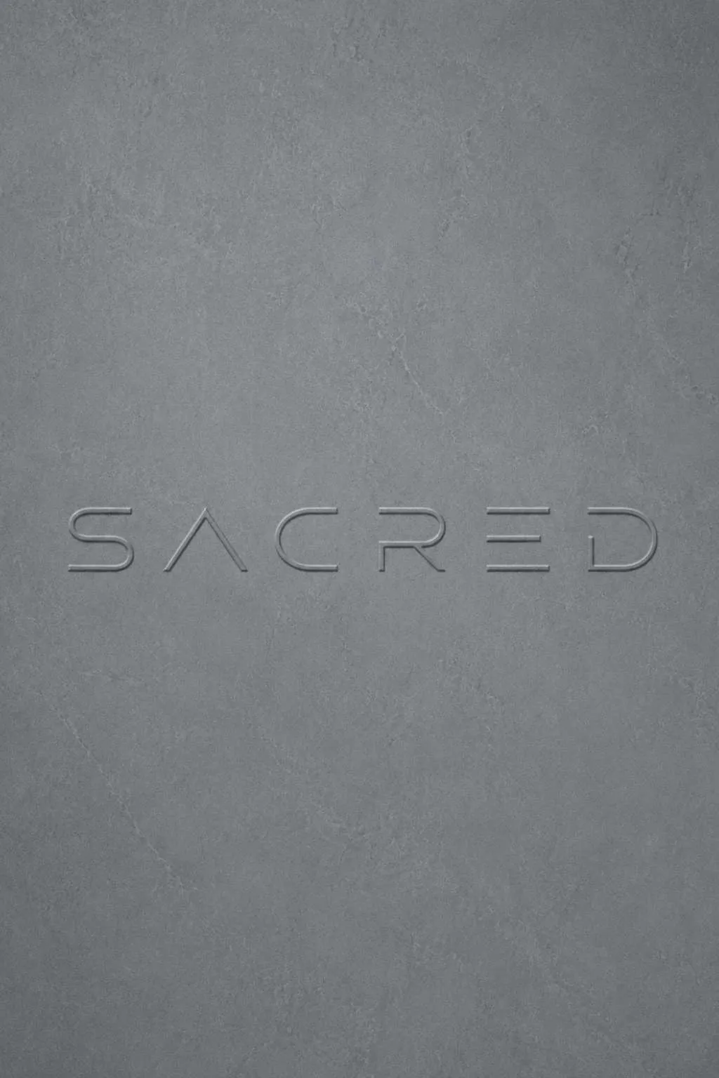 SACRED wordmark embossed on soft grey stone – ethical fashion house