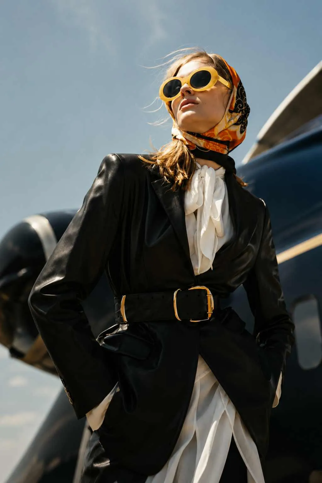 Woman in yellow sunglasses and silk headscarf beside a private jet